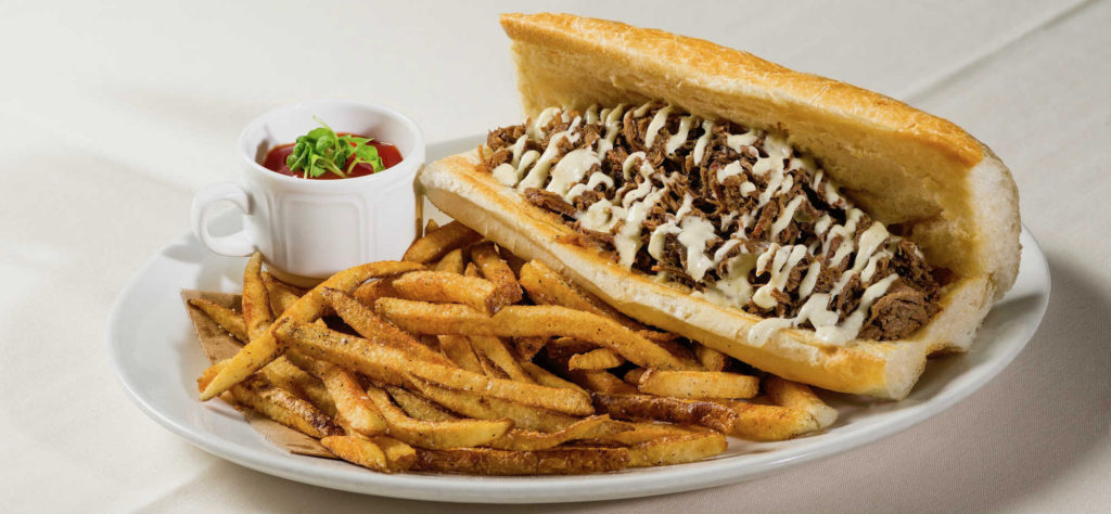 Sub sandwich with shredded beef and sauce, served with fries and a cup of ketchup on a white plate. Prime Rib sandwich with shredded beef and sauce, served with fries and a cup of ketchup on a white plate.
