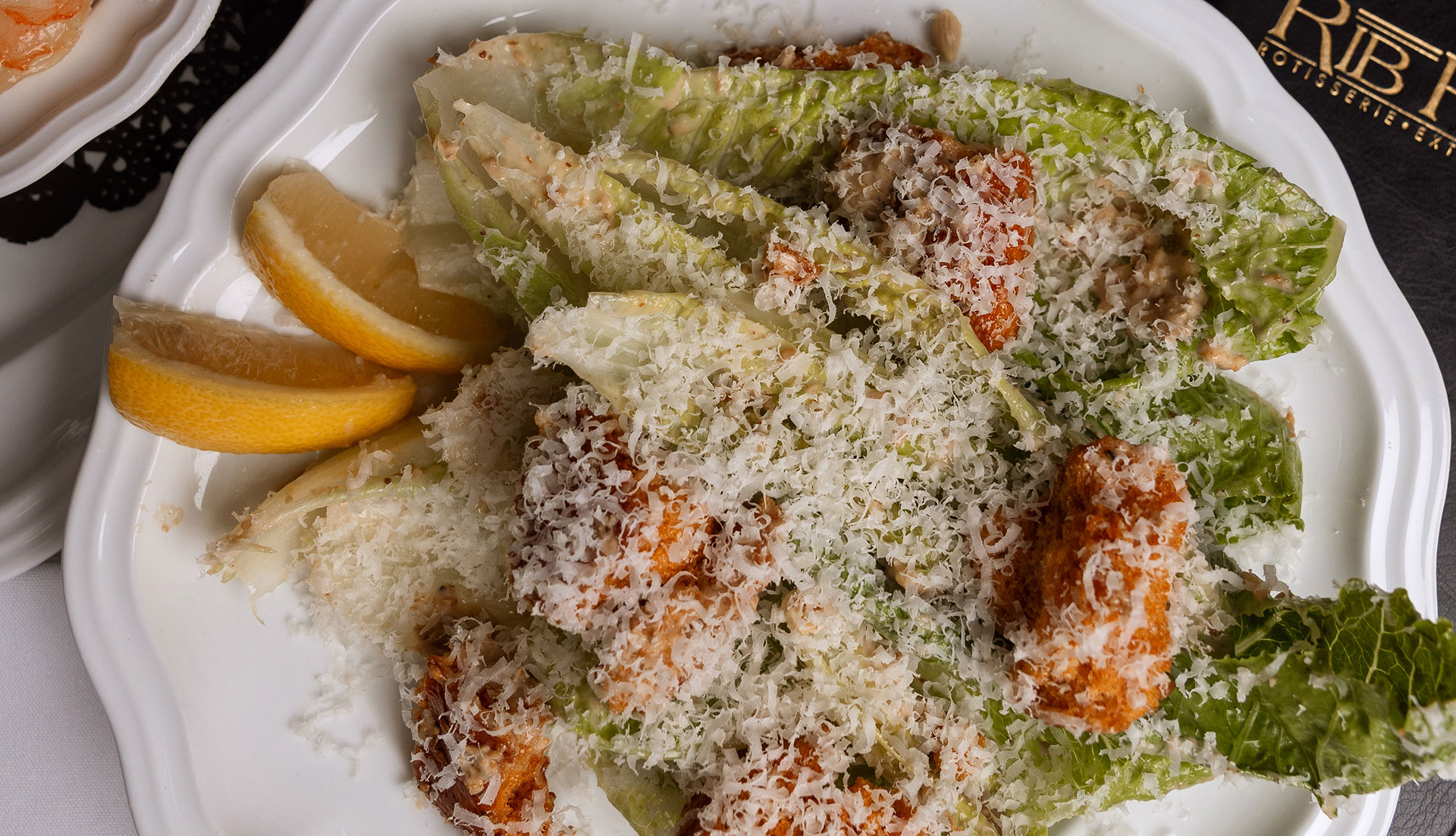 A plate of Caesar salad with romaine lettuce, croutons, grated cheese, and lemon wedges on a white plate.